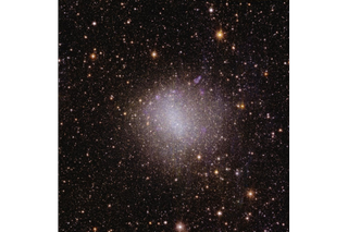 A sparkling pinkish and white spot of light in the center of the image, surrounded by millions of dots of light representing distant cosmic objects.