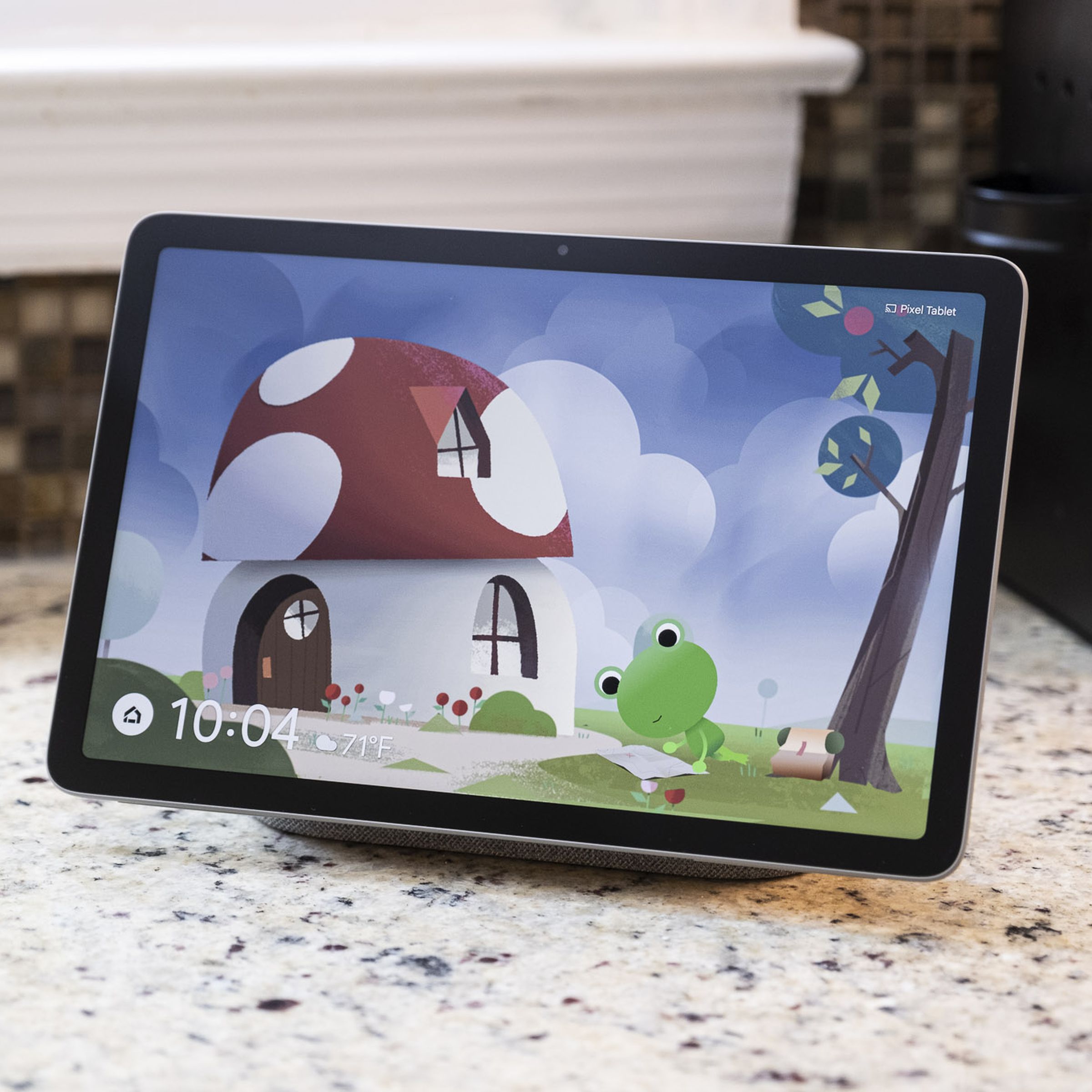 A Pixel Tablet mounted on a docking station with a speaker displaying the Weather Frog screensaver.