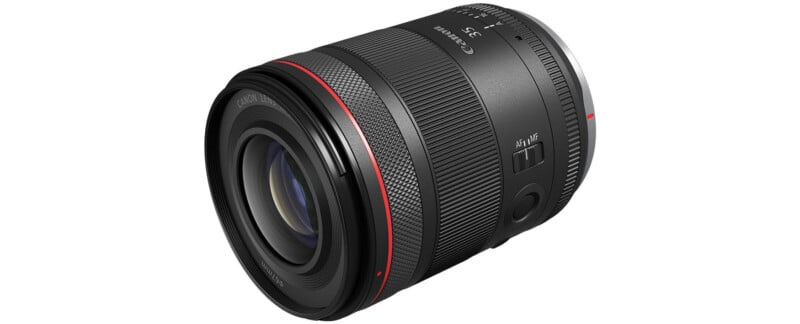 A black Canon RF 35mm f/1.8 IS Macro STM lens is shown on a white background.  The lens is equipped with a wide focus ring, a control ring and an image stabilization switch.  It has a red ring near the front element to indicate its L-series status.