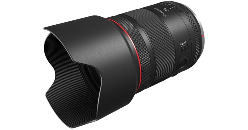 A Canon camera lens with a black body and a red ring on the front.  The lens has a knurled focus ring, switch button, and a fitted sun visor to protect the lens.  The Canon logo and specifications are visible on the lens body.