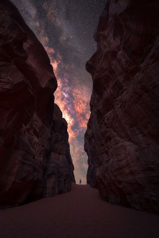 The Milky Way photographed between two high cliffs with a lone man standing in the middle