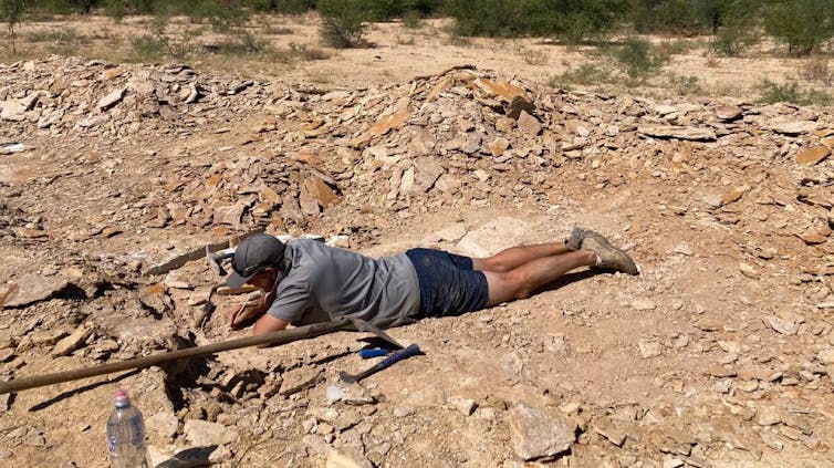 Photo of a man lying on his stomach and digging in the dirt