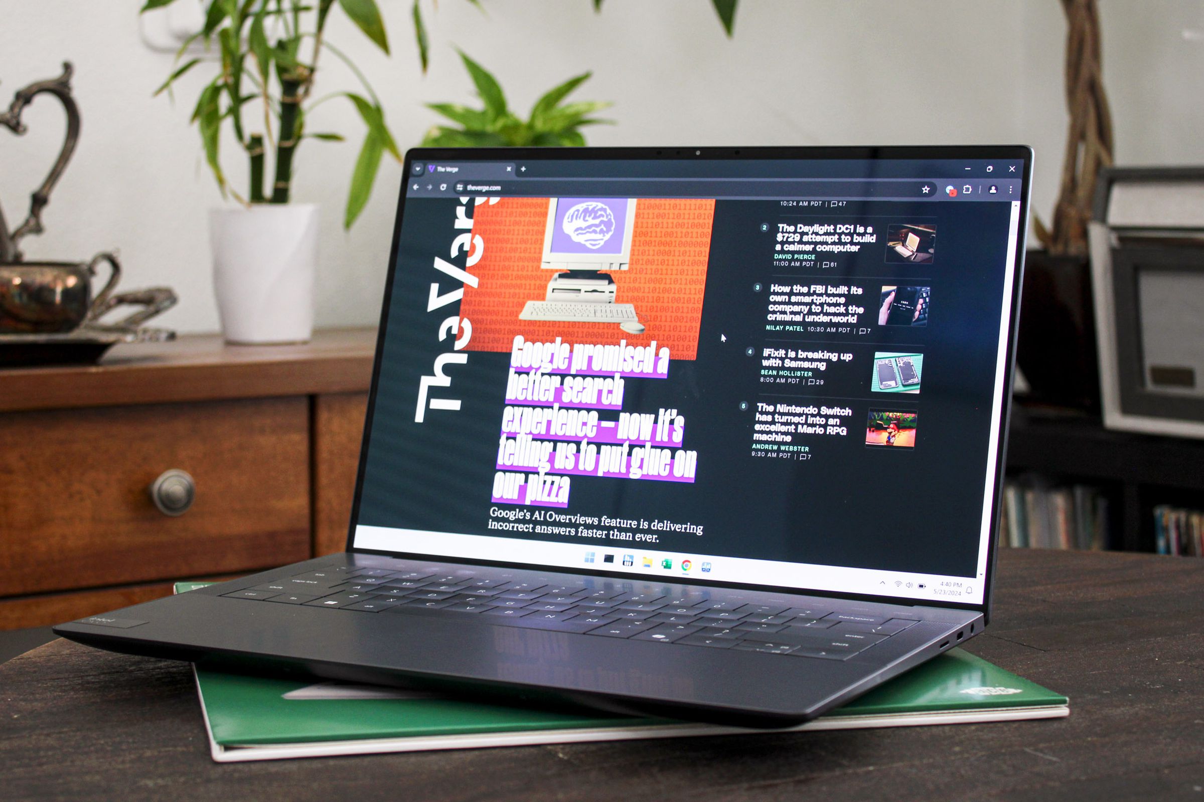 An open and switched on laptop sitting on a wooden table with plants and furniture in the background.