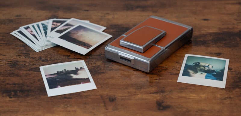 A collection of instant photos scattered on a wooden surface.  On the right is a dog in one photo.  In the center is a vintage instant camera with a brown leather cover.  Additional photos are partially visible in two piles to the left of the camera.