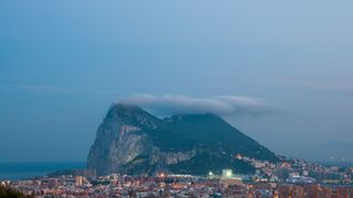 The Rock of Gibraltar at dusk with the Levante Cloud forming above it.  In the foreground is the sprawling border town of La Linea de la Concepción, Cádiz, Spain.