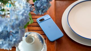 A blue Google Pixel 8a on a tea tray with blue hydrangeas above it