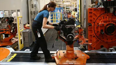 Getty Images A woman works on a black and orange machine in a factory