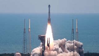 a white rocket takes off on a sunny day above a cloud of fire and smoke