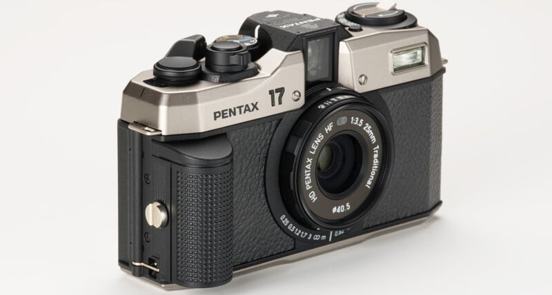 A silver and black Pentax 17 camera with a 12.5mm f/3.5 lens is shown against a white background.  The camera has a textured grip, multiple control dials on the top, a viewfinder and flash on the front right above the lens.