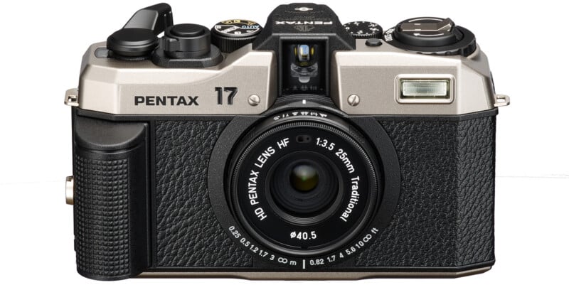 Pentax 17 camera in retro style with black and silver body.  The camera has a large central lens marked "HD lens Pentax HF 1:3.5 25mm traditional" and several control wheels and buttons on the top.  The front features textured grip areas and a built-in flash.