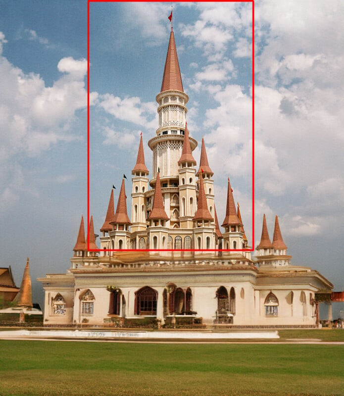 A large Thai temple with an ornate central tower and four surrounding smaller towers against a background of blue sky and clouds.  The temple is richly decorated and surrounded by lush green lawns and other traditional structures.