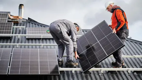 Getty Images Two men work to attach solar panels to the roof