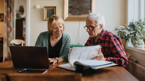 Getty Images A retired couple looks over their finances on paper and a laptop