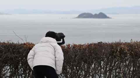 A man looks through binoculars at the North Korean coast from a viewpoint in South Korea