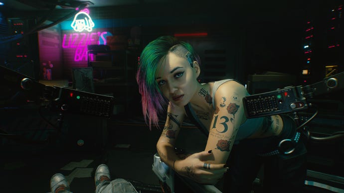 Judy leans over the player while sitting in the Braindance studio in Cyberpunk 2077.