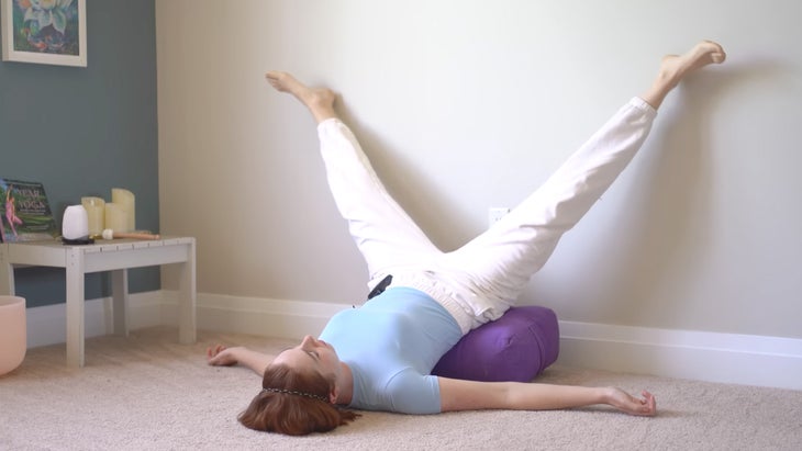 a woman practices yoga against a wall with her legs in a narrow split