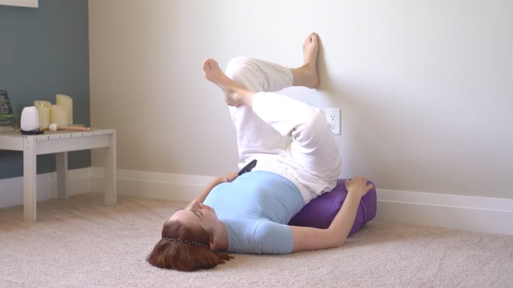 a woman practices yoga against a wall with one foot on the wall