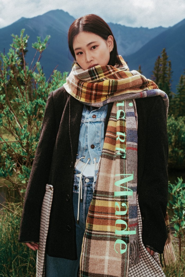 A woman in the countryside wears a checkered scarf and a dark jacket