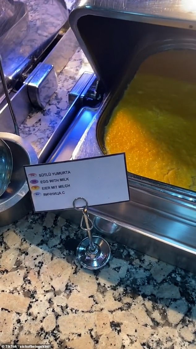 Image from the video: A tray of scrambled eggs served with milk.  Each of the breakfast items was labeled in different languages