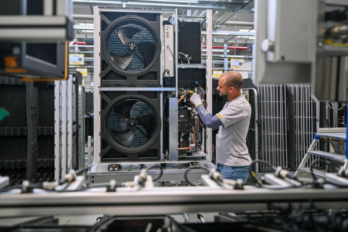 A gloved technician works on a large industrial HVAC unit, adjusting wires and components, two large fans are seen inside the unit