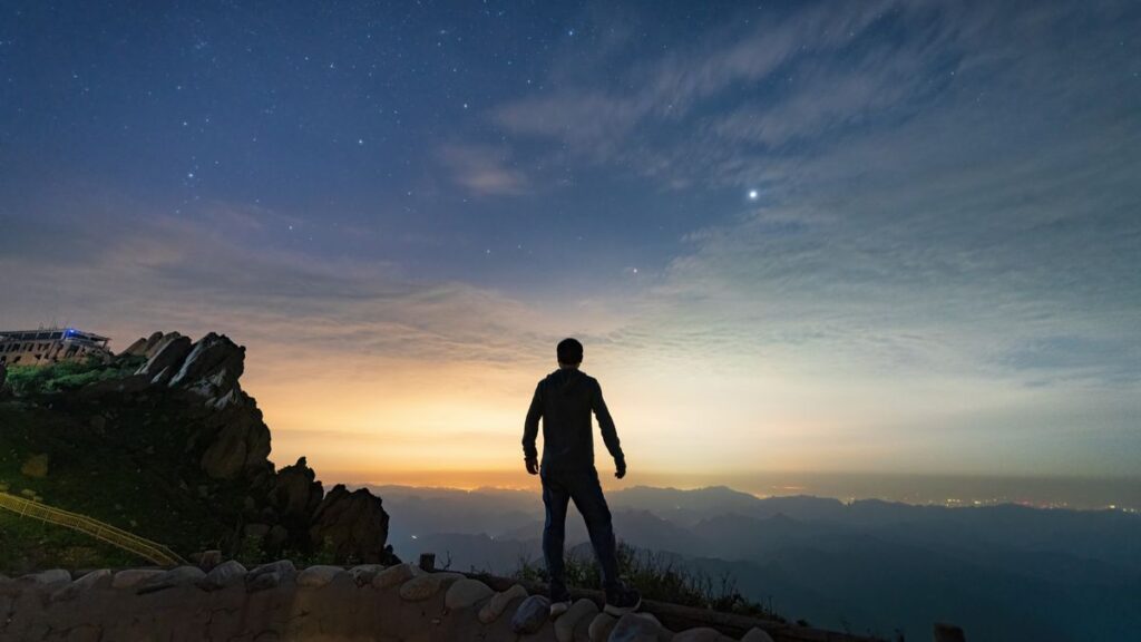 man looks down on the night view of the city at the top of the mountain