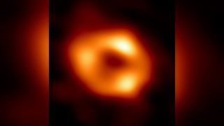 telescopic image of a black hole, revealed as a blurry donut of yellow-orange light surrounding a black center